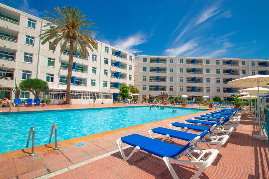 a swimming pool with lounge chairs and a hotel at Apartamentos Tamaragua in Playa del Ingles