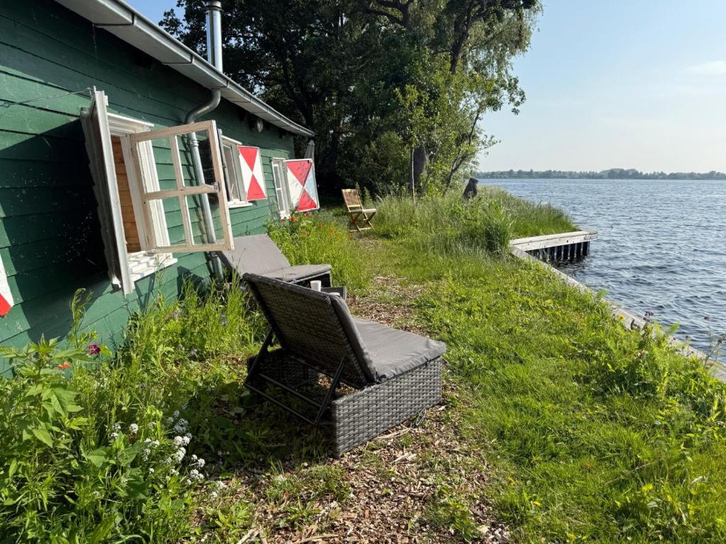 a chair sitting outside of a house next to the water at The Historical Trick Hut in the middle of the Lake in Baambrugse Zuwe
