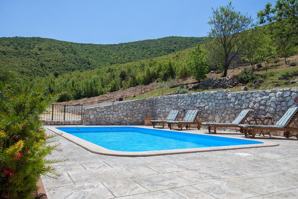 a swimming pool with benches and a stone wall at Holiday Villa Anna in Primorski Dolac