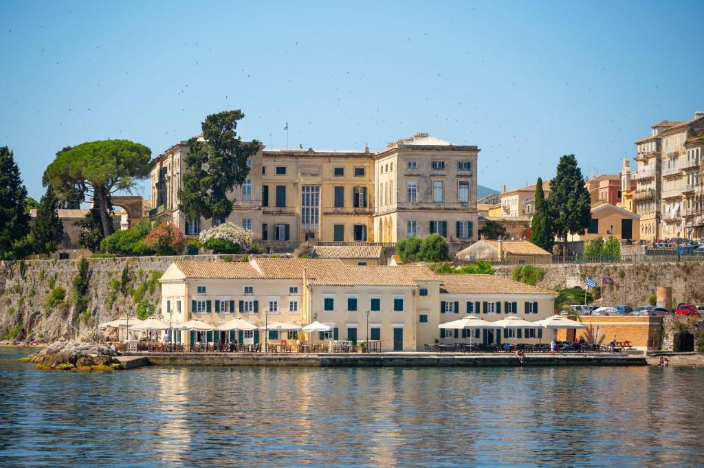 un groupe de bâtiments à côté d'une masse d'eau dans l'établissement Suite Semiramis, à Corfu