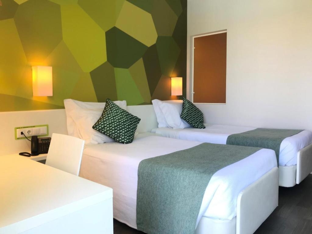 two beds in a hotel room with a colorful wall at Hotel 3K Faro Aeroporto in Faro