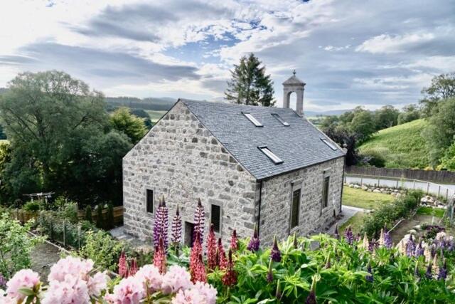 Una iglesia de piedra con una torre de reloj en un jardín. en Church Brae, en Tomatin