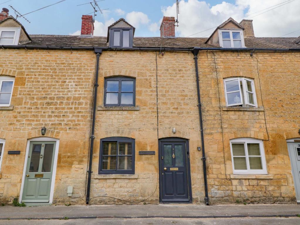 una vecchia casa di mattoni con porte e finestre verdi di Elm Cottage a Moreton in Marsh