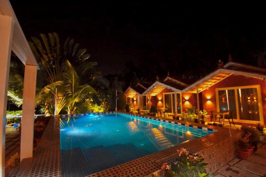a swimming pool in front of a house at night at Golden Rice Resort & Cottages in Candolim