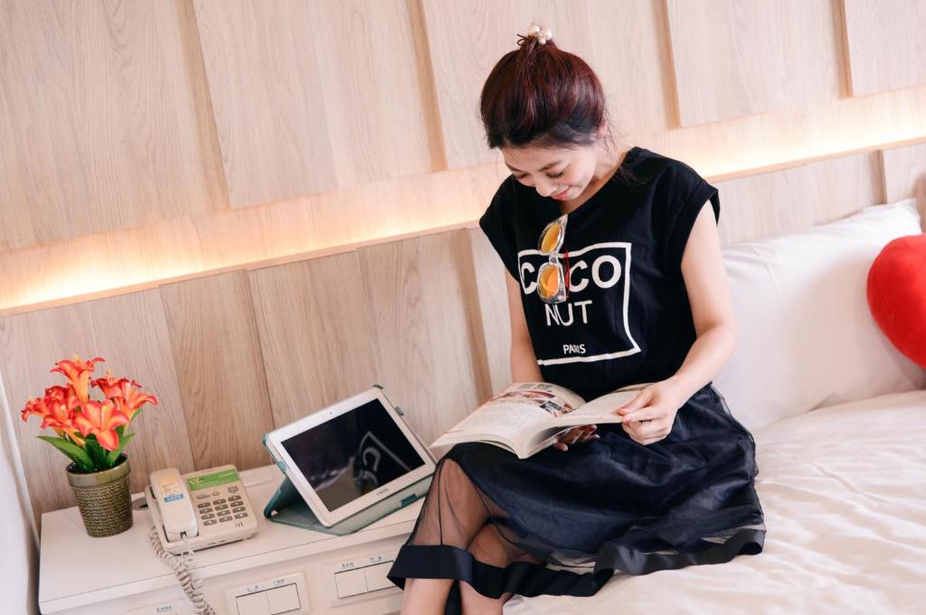 a woman sitting on a bed reading a book at KIWI-Taichung Station Branch 1 in Taichung