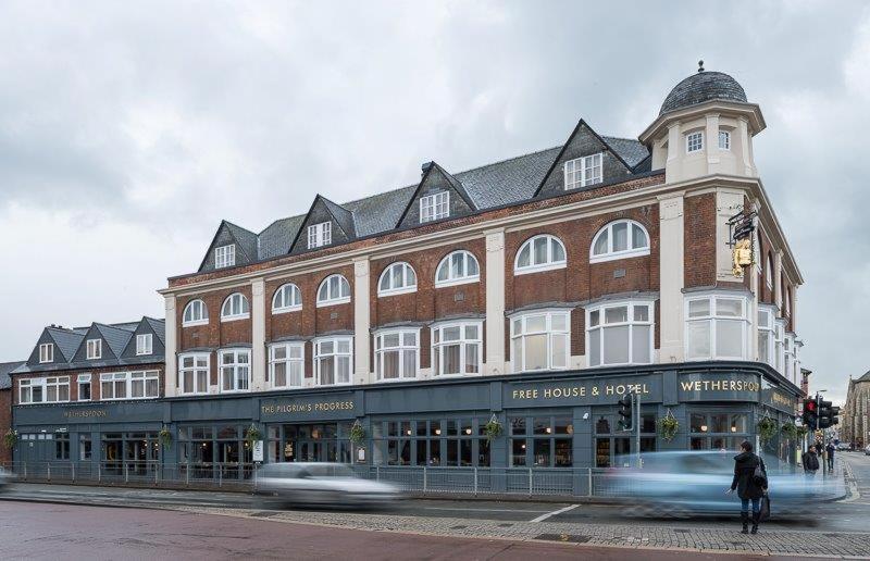 un gran edificio en una calle con autos pasando por ella en Pilgrims Progress Wetherspoon en Bedford