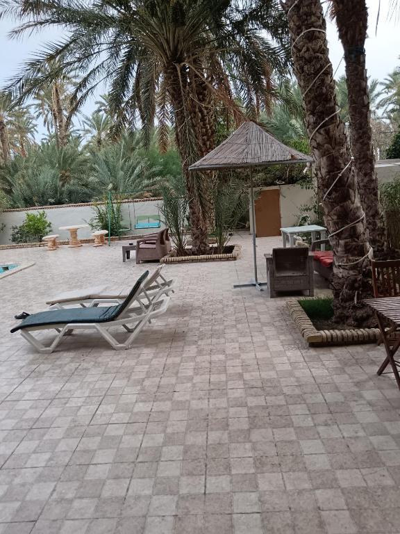a patio with chairs and an umbrella and palm trees at Résidence Loued in Tozeur