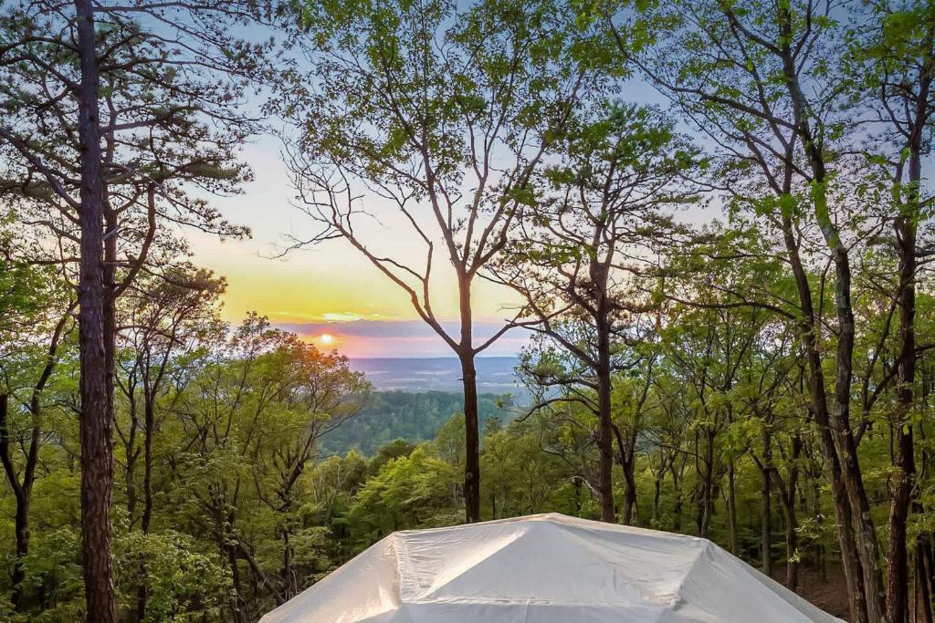 a tent in the woods with the sunset in the background at Cozy Chalet & Luxe Domes Retreat w Stunning Views in Augusta