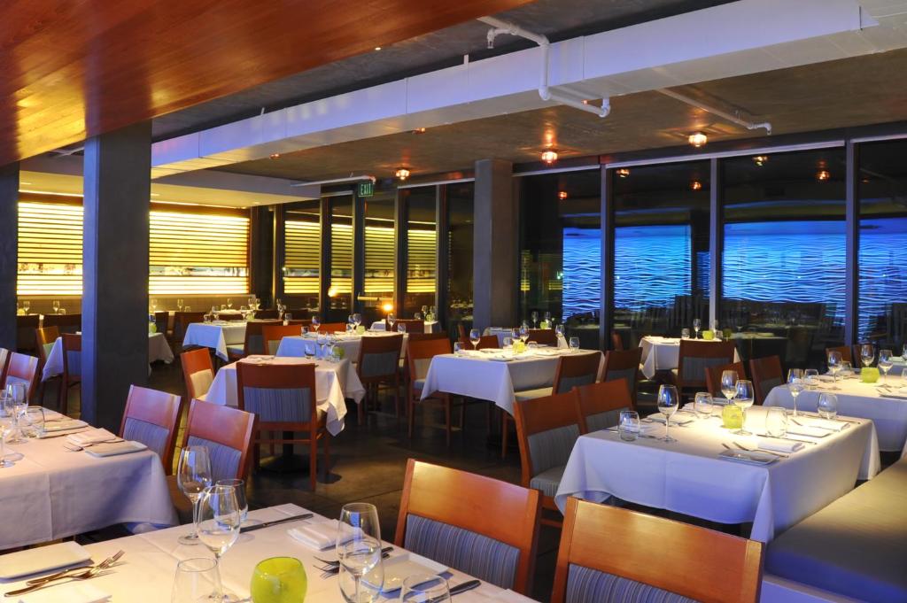 a restaurant with white tables and chairs and windows at Tower 23 Hotel in San Diego