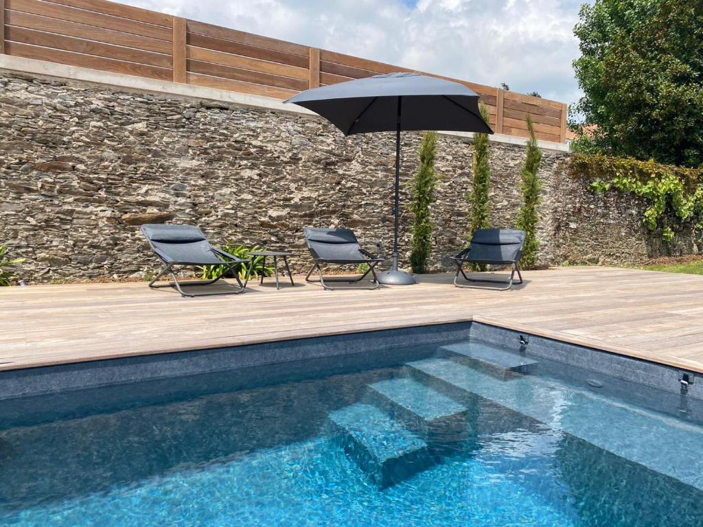 un patio avec deux chaises et un parasol à côté d'une piscine dans l'établissement Le Clos de Jade - Appt 3 étoiles avec piscine partagée, à Pornic