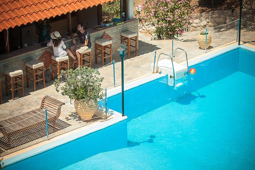 two people sitting at a table next to a swimming pool at Porto Koufo Resort in Porto Koufo