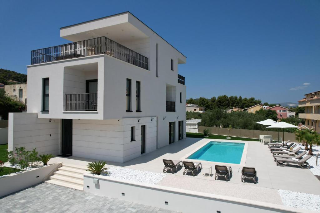 een groot wit huis met een zwembad en stoelen bij Villa Perla auf Ciovo in Slatine