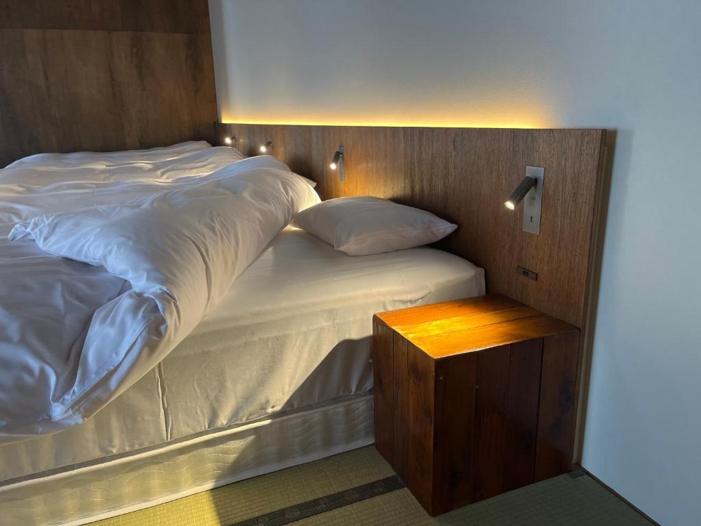 a bed with white sheets and a wooden head board at 古民家ラグジュアリーホテル 金井西洋館 in Sado