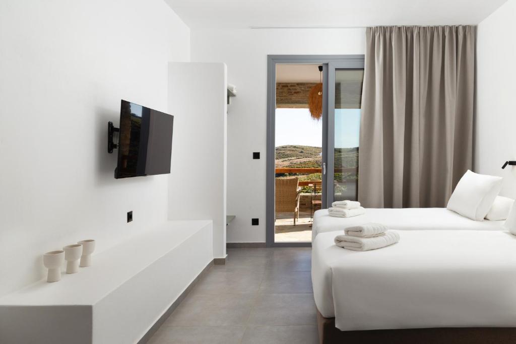 a white room with two beds and a television at Spanos Apartments in Agios Petros