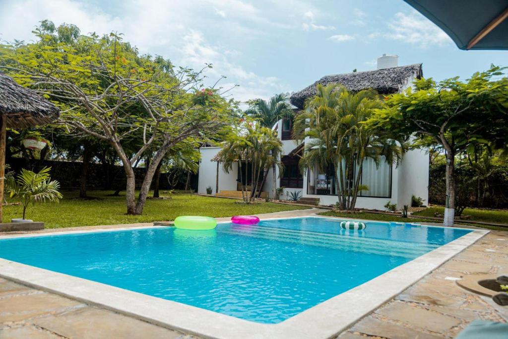 a swimming pool in front of a house with trees at Seb Villa in Diani Beach