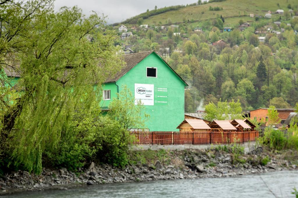 a green building with a fence next to a river at Dream Hostel Carpathians Rakhiv in Rakhiv