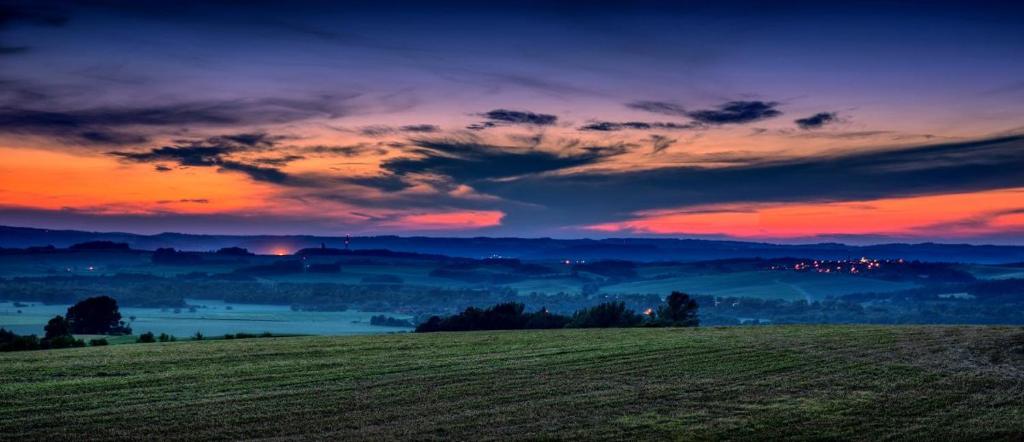 a field with a sunset in the background with a sky at Karavan na samotě u lesa 