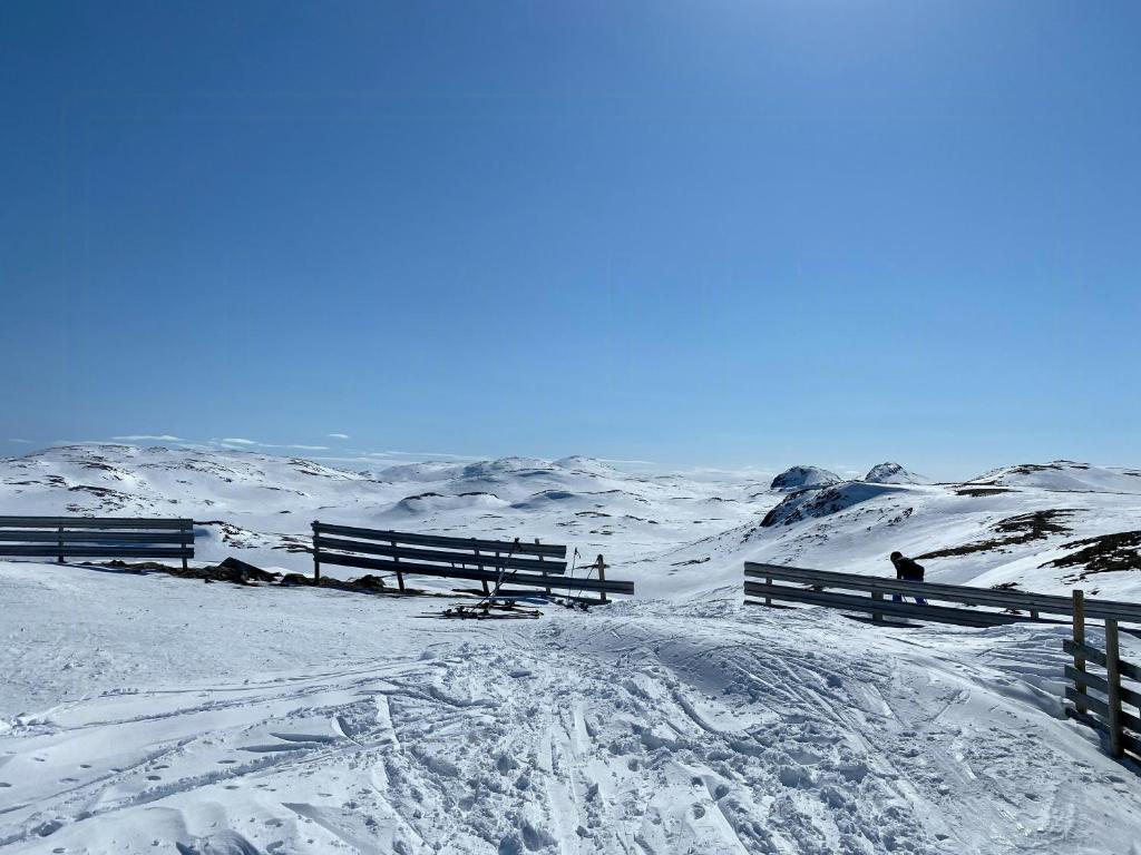 a snow covered hill with a fence and a person in the distance at Luksuriøs Bjælkehytte Af Hardangervidda in Uvdal