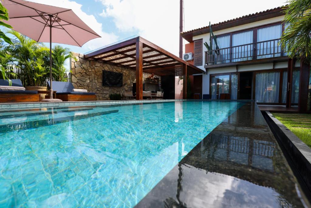 a swimming pool in front of a house with an umbrella at Casa dos Corais Patacho in Pôrto de Pedras