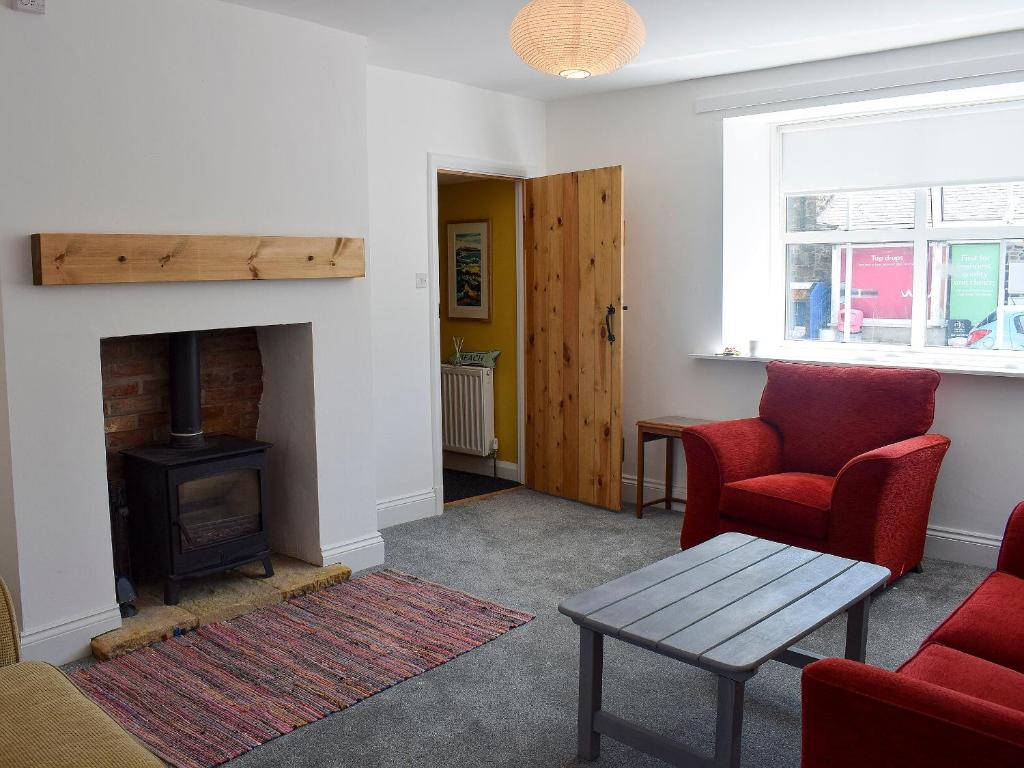 a living room with a fireplace and red chairs at Alice Cottage in Embleton