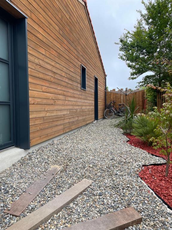 a house with a wooden wall and a gravel driveway at mini villa neuve moderne proche des plages in Brétignolles-sur-Mer