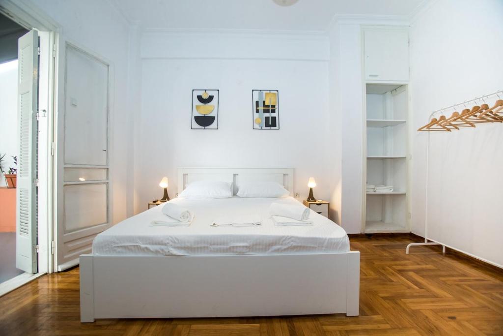 um quarto branco com uma cama branca e pisos em madeira em Athens Central Jacuzzi Retreat em Atenas
