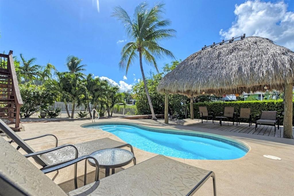 a resort swimming pool with chairs and a straw umbrella at Kon Tiki - Waterfront Pool Home Near Sombrero Beach, 30' Dock, Tiki Hut in Marathon
