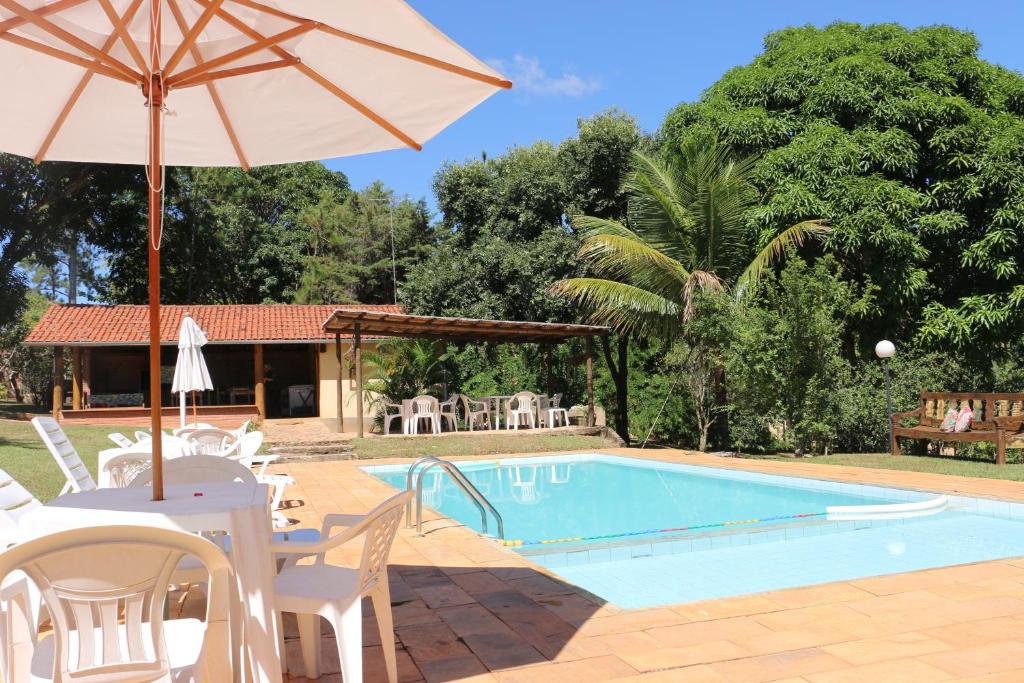 a swimming pool with an umbrella and a table and chairs at Pousada Alto do Bau in Conceição do Mato Dentro