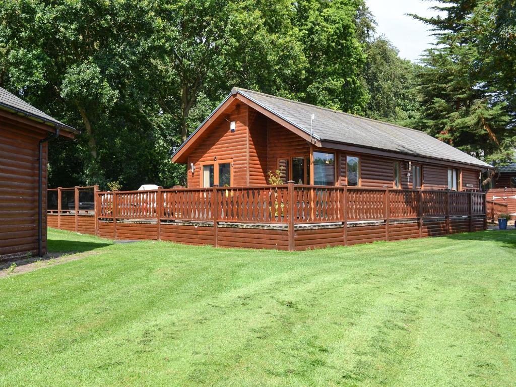 a wooden cabin with a fence and a yard at Pine Lodge in Sewerby