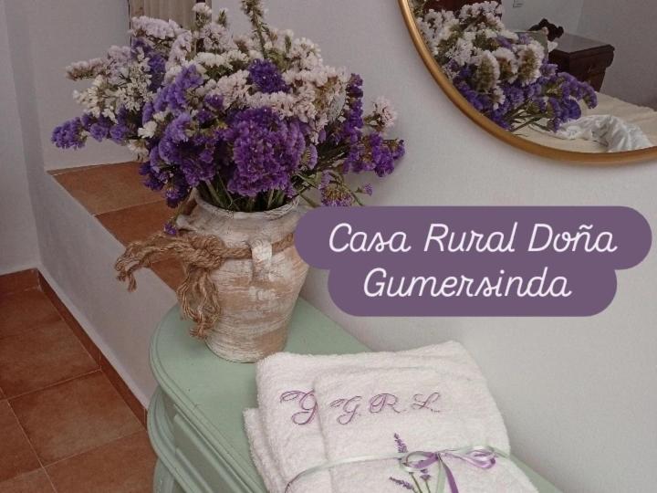 Un jarrón de flores moradas sobre una mesa con un espejo. en Casa Rural en San Carlos del Valle- Doña Gumersinda, en San Carlos del Valle