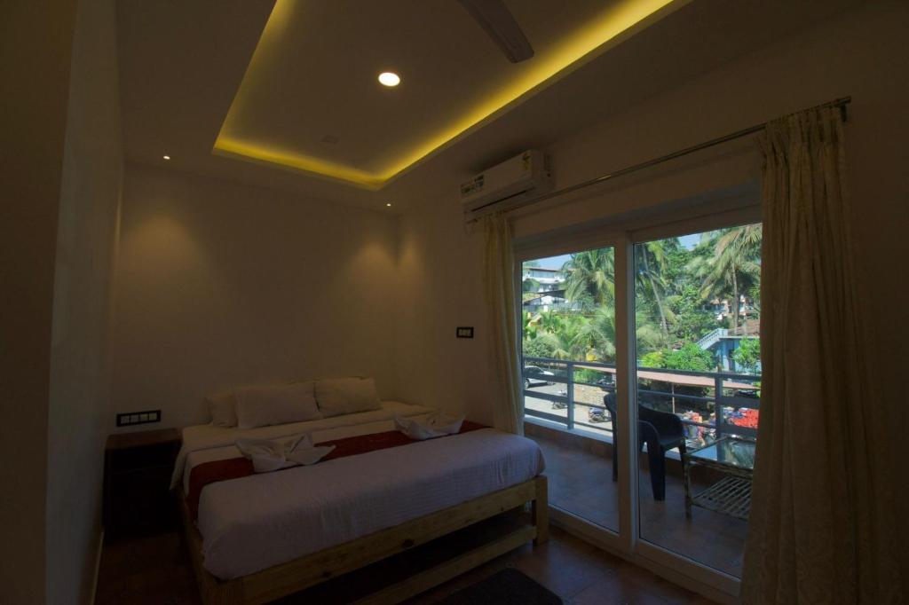 a bedroom with a bed and a balcony with a window at Golden Rice Resort & Cottages in Candolim