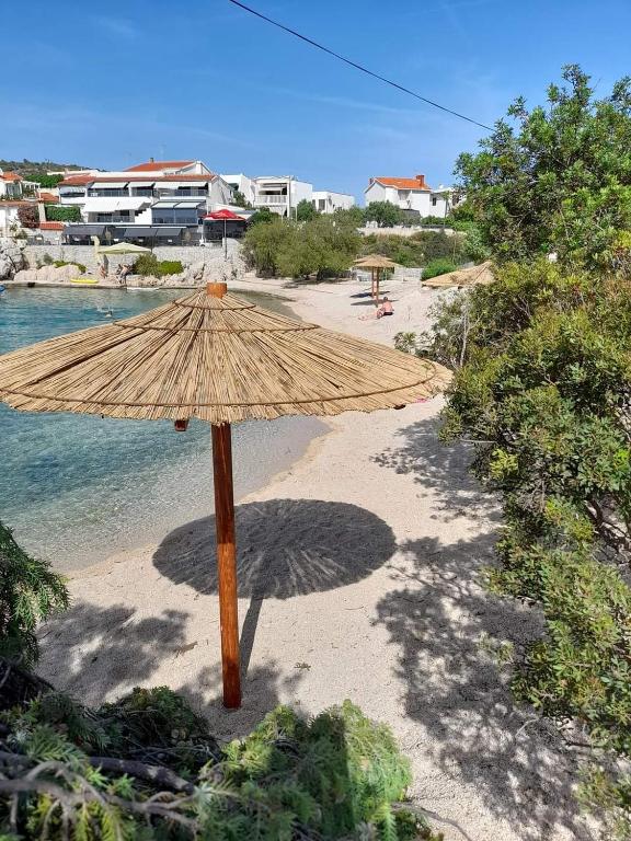 a straw umbrella sitting on a beach next to the water at Apartmani Versizo Rogoznica in Sevid