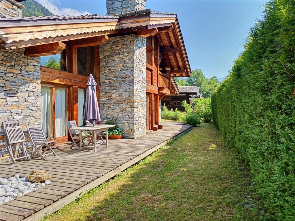 une maison dotée d'une terrasse en bois avec une table et un parasol dans l'établissement Chalet Spacieux à Chamonix pour 9 – Vue Panoramique Mont-Blanc, Jacuzzi, Jardin & Parking, à Chamonix-Mont-Blanc