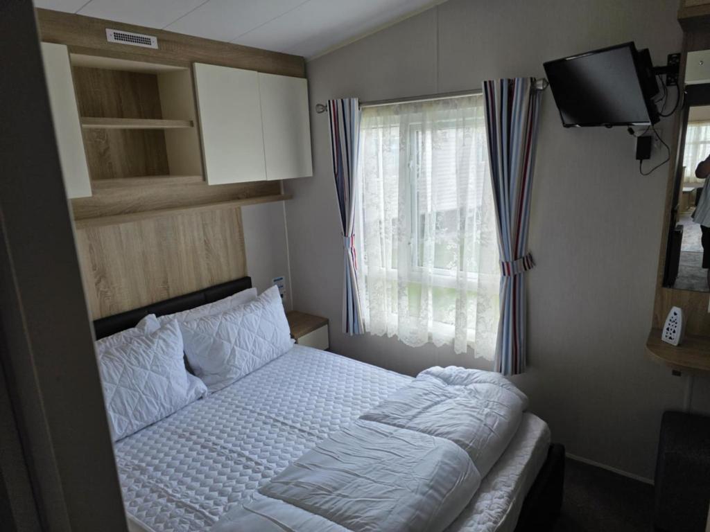 a small bedroom with a bed and a window at PALM GROVE THE NeW PG68 3 BEDROOM CARAVAN CHAPEL ST LEONARDS in Chapel Saint Leonards