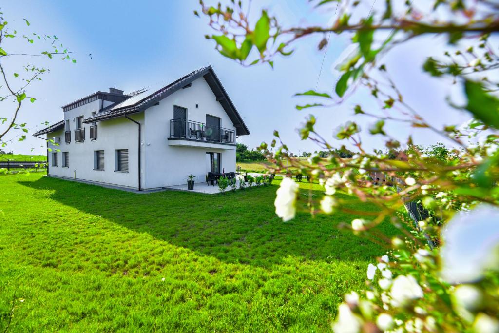 a white house on a grassy field with a tree at Horyzont Apartamenty Zator in Gierałtowiczki