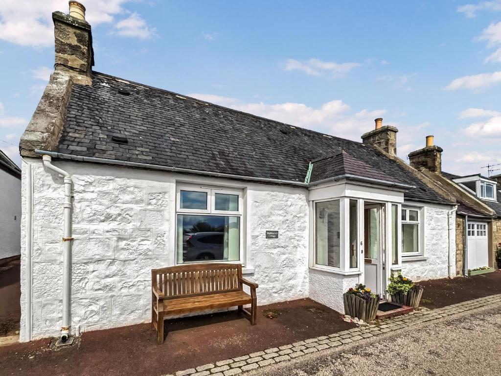 una casa de campo blanca con un banco delante en Middledrift Cottage, en Brora