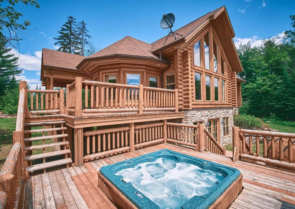 a log home with a hot tub on a deck at Forest Getaway, Soak in the Spa, Sauna, Fireplace in Mille-Isles