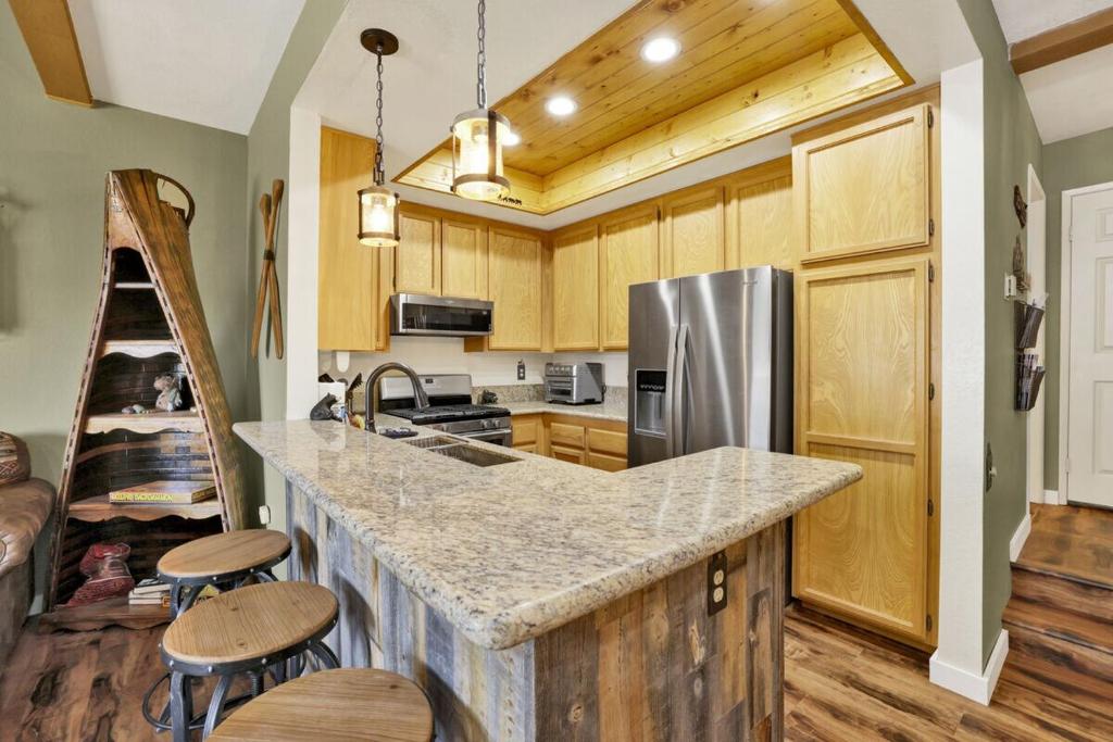 una cucina con mobili in legno e un bancone con sgabelli di Boulder Bear Lakeside Condo- Big Bear Modern Retreat a Big Bear Lake