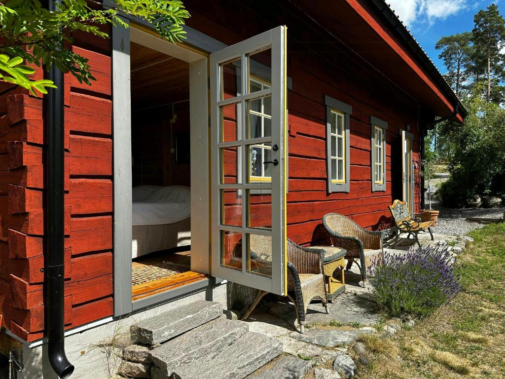 a red cabin with a door and chairs outside at Unique Log Cabin With Sea View In Trosa in Västerljung