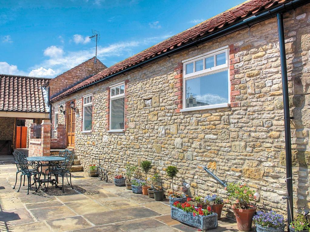 a stone house with a table and chairs and plants at Stable Cottage in Burythorpe