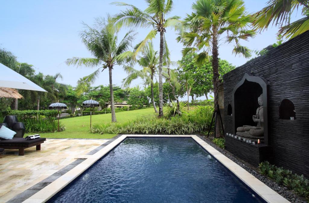 a swimming pool in front of a house with palm trees at Villa Arjuna in Tanah Lot