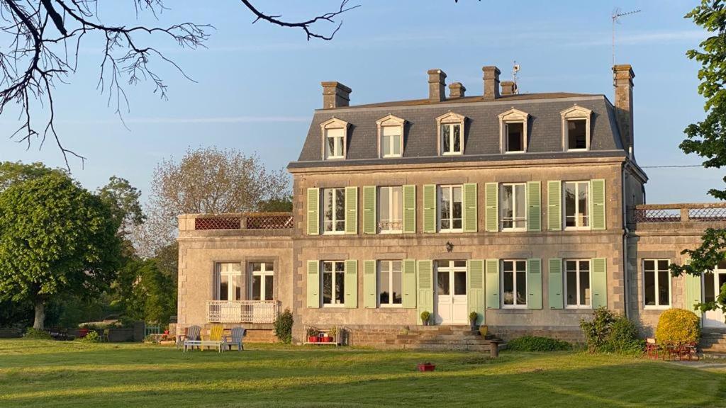 a large house with green shutters on a grass field at l'appart de la Maison du Hommeel in Gratot