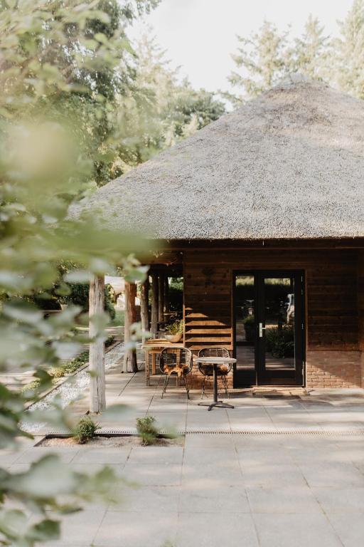 a cabin with a thatch roof and a patio at B&B Mollenvlied Veluwe in Vaassen
