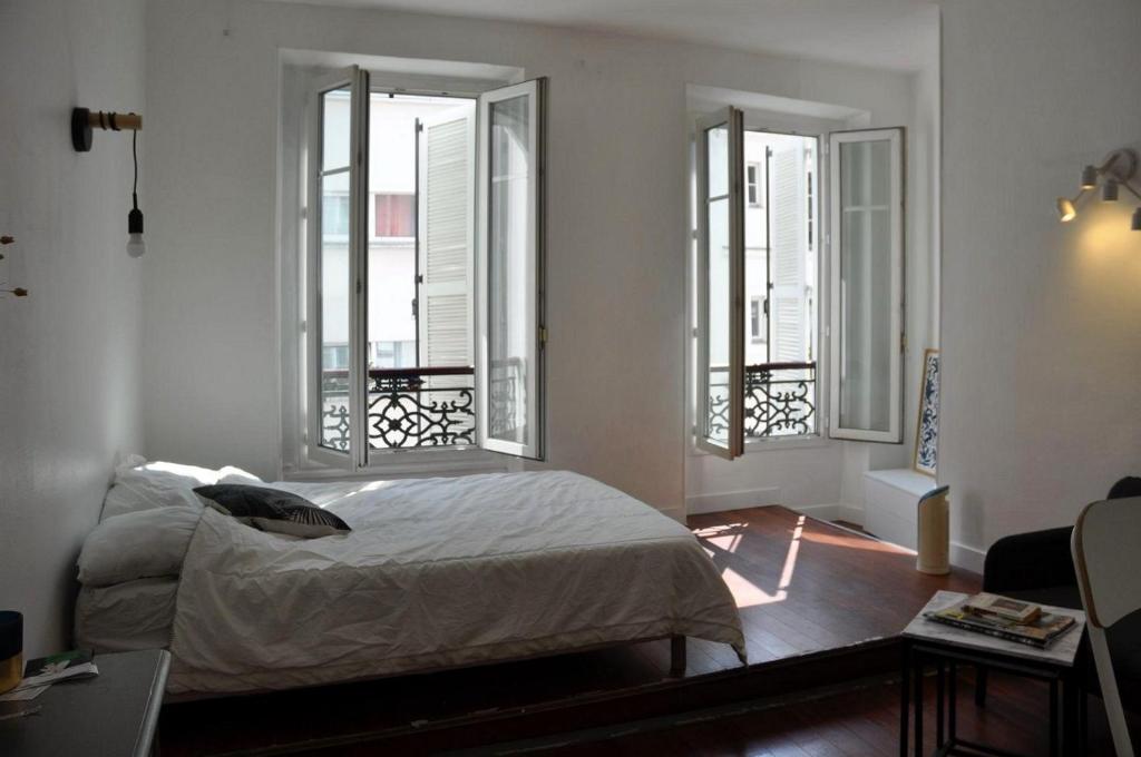 une chambre avec un lit et deux fenêtres dans l'établissement Appartement Buttes Chaumont, à Paris