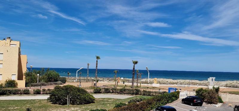 - une plage avec des palmiers, un bâtiment et l'océan dans l'établissement appartement port barcares, au Barcarès