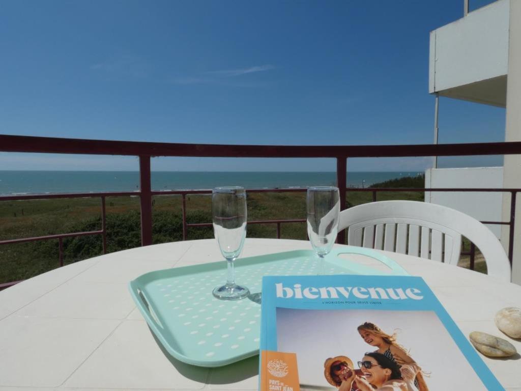 une table avec un magazine et des verres sur un balcon dans l'établissement Appartement cosy à Notre-Dame-de-Monts pour 2 personnes - FR-1-540-324, à Notre-Dame-de-Monts