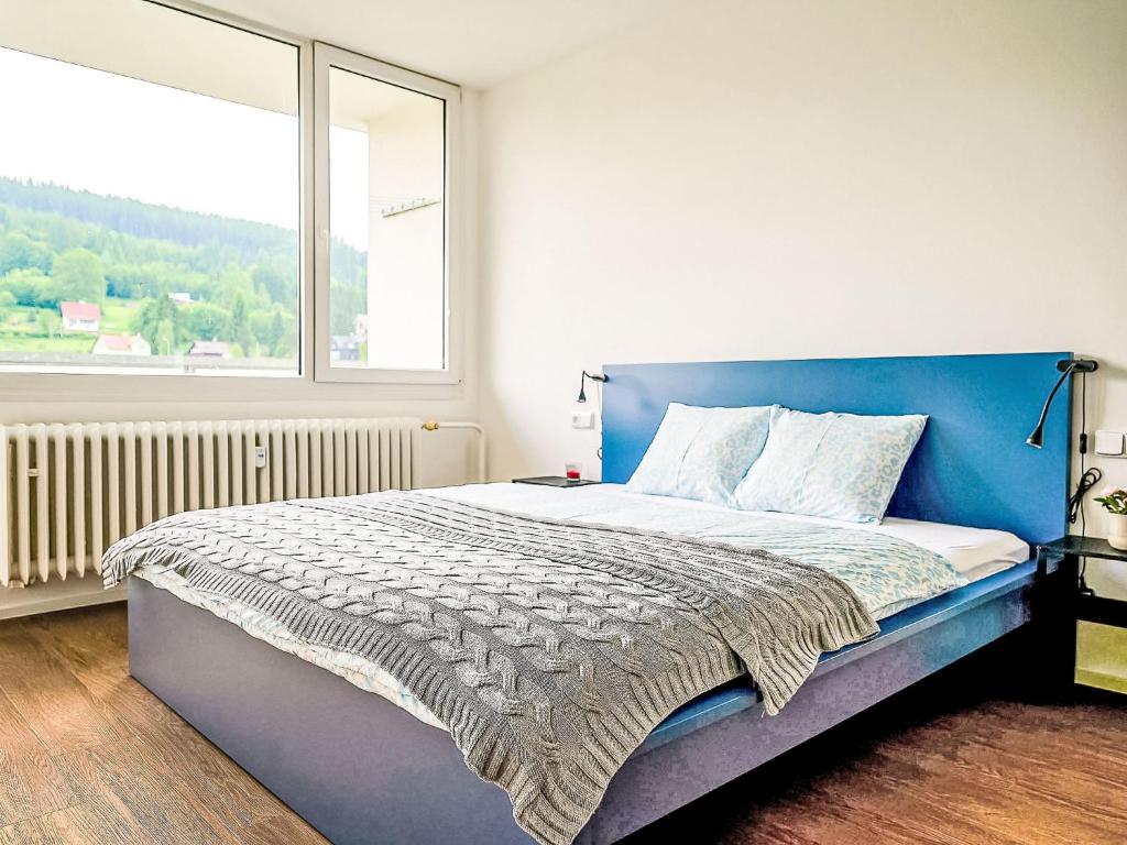a bedroom with a blue bed with a large window at Apartment Forest line by Interhome in Josefŭv Dŭl