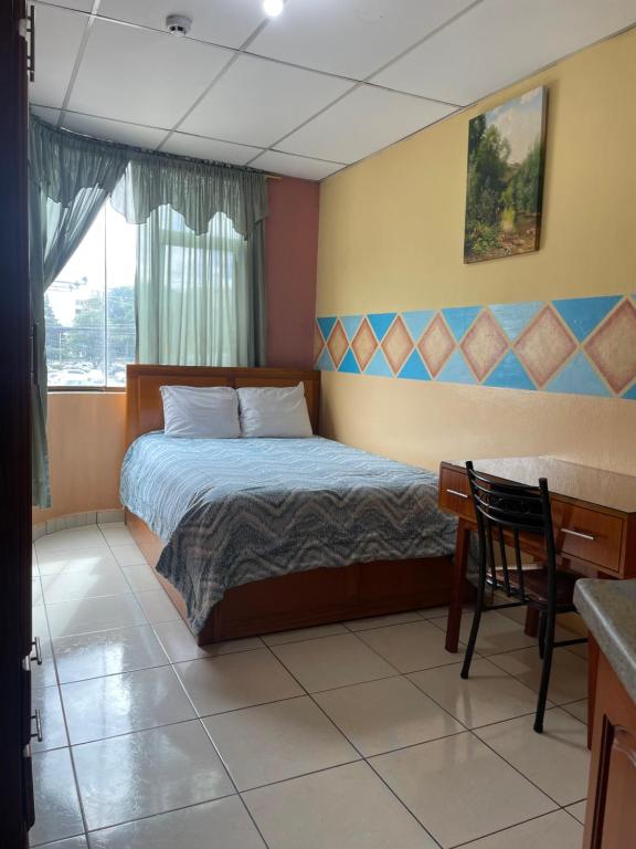 a bedroom with a bed and a desk and a window at Hostal Abu Dhabi in Cuenca