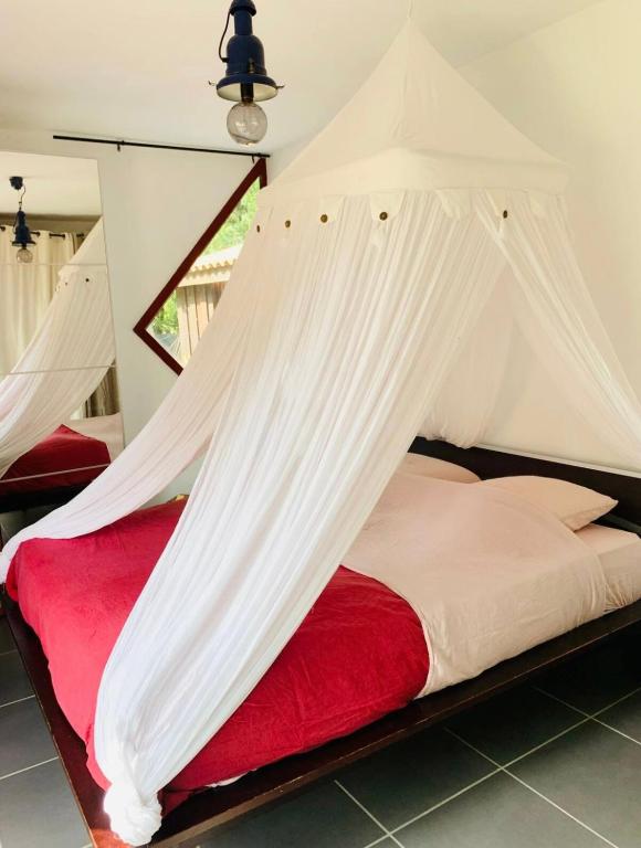 une chambre avec un lit rouge avec des moustiquaires blanches dans l'établissement La Balinaise, à Hourtin