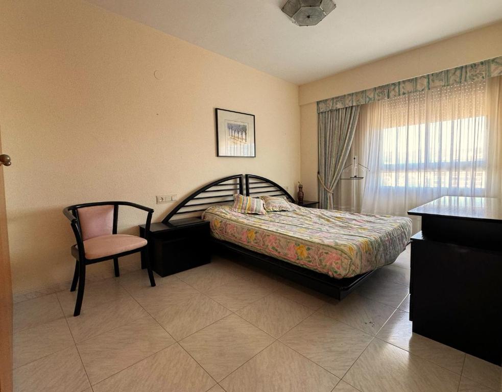 Un dormitorio con una cama y una silla y una ventana. en Tropicana, en Benicàssim